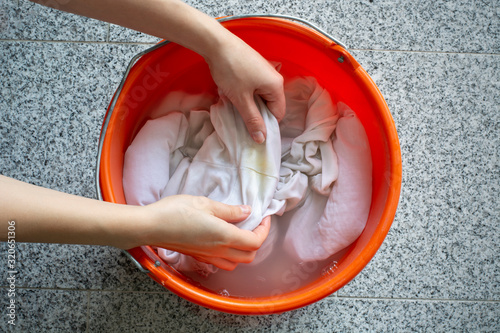 Cleaning laundry manually. Women's hands washing dirty white shirts with yellow sweat stains to soak it in a bucket