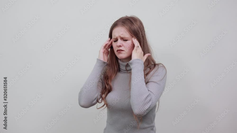 a young beautiful red haired woman in gray sweater is suffering from headache she is holding hand on head