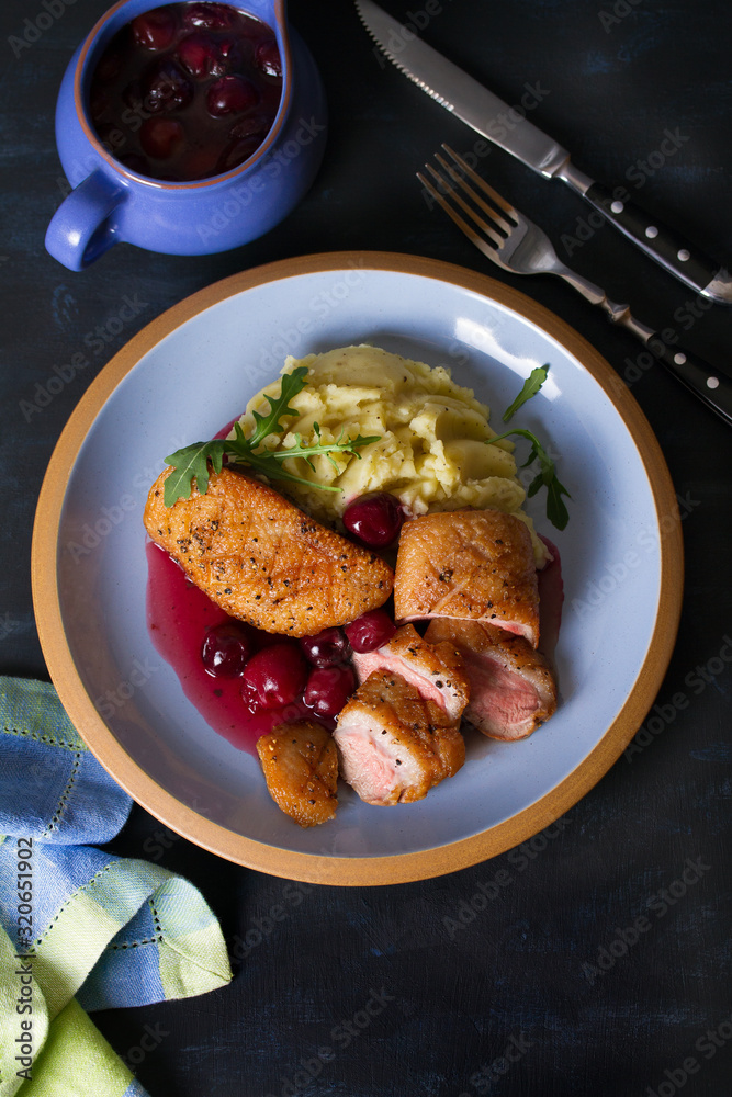 Duck breast fillet with cherry wine sauce and mashed potato on blue plate, dark background. Overhead Vertical image Duck breast fillet with cherry wine sauce and mashed potato on blue plate, dark background. Overhead Vertical image