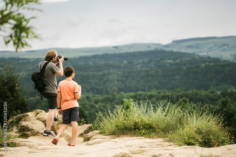 Father and son taking pictures in the mountains and admiring the beautiful landscape. Man and boy travelers together