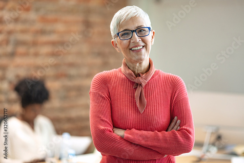 Pretty older business woman, successful confidence with arms crossed in financial building. Cheerful attractive businesswoman crossing arms on chest and looking at camera. photo