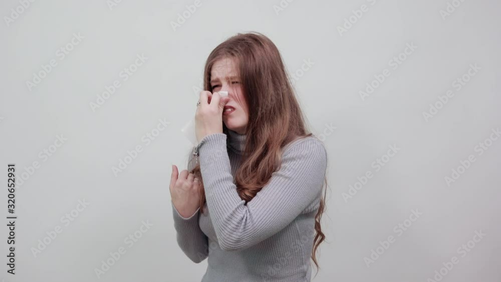 a young beautiful red-haired woman in gray sweater wipes her nose with handkerchief because she has runny nose snot is flowing. Cold, illness a young beautiful red-haired woman in gray sweater wipes her nose with handkerchief because she has runny nose snot is flowing. Cold, illness
