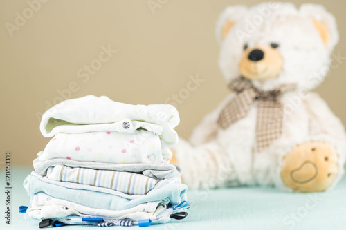 stack of pressed, ironed newborn baby clothes  with a plush teddy bear photo