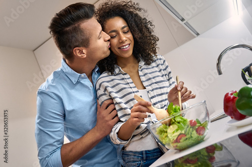 Young adult mixed race couple kissing, cooking healthy food together