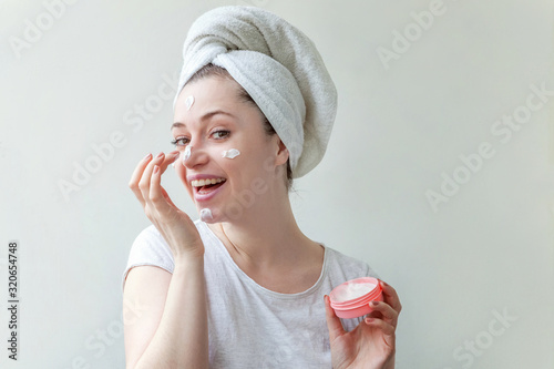 Beauty portrait of woman in towel on head with white nourishing mask or creme on face, white background isolated. Skincare cleansing eco organic cosmetic spa relax concept. photo