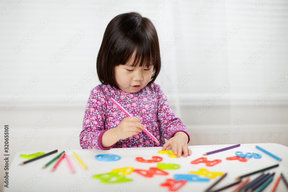 toddler girl practice writing letters on white paper against white background toddler girl practice writing letters on white paper against white background