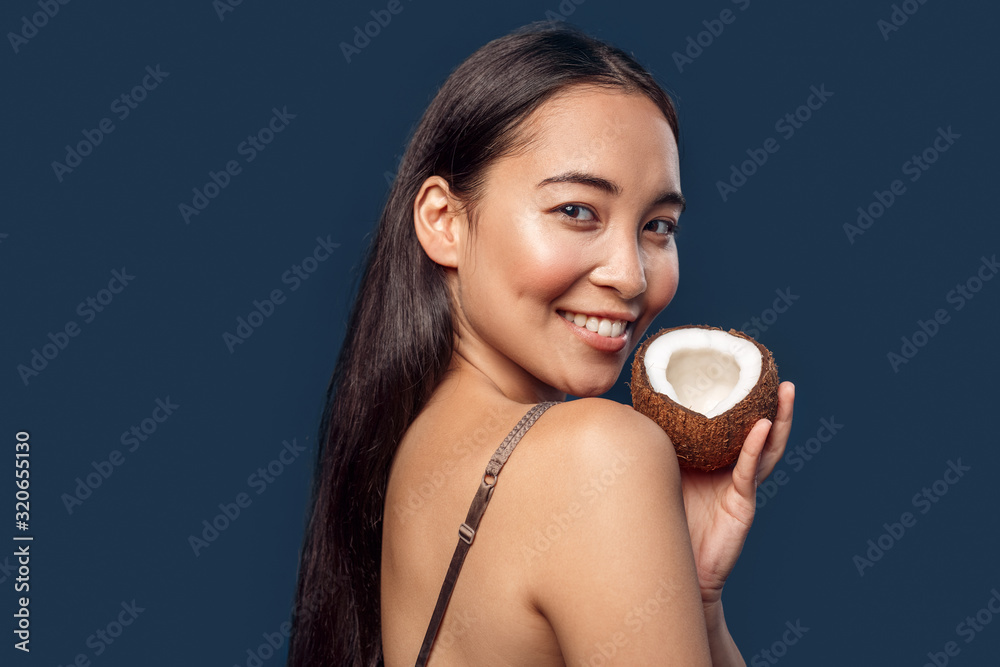 Freestyle. Young woman standing isolated on blue holding coconut smiling toothy close-up Freestyle. Young woman standing isolated on blue holding coconut smiling toothy close-up