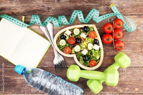 Authentic fresh salad in a wooden heart shaped cup with dumbbells excercise equipment, measuring tape on table. healthy lifestyles, good health photo