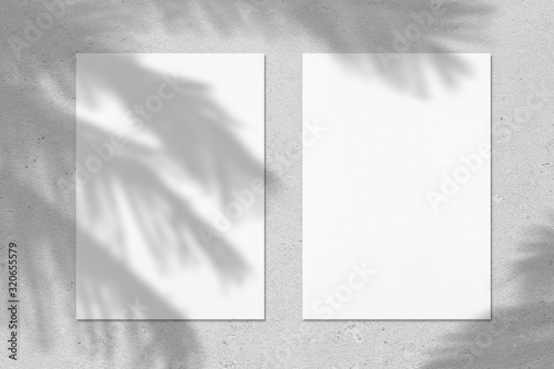 Two empty white vertical rectangle poster or business card mockups with with palm leaves shadows on soft grey concrete background. Flat lay, top view. 