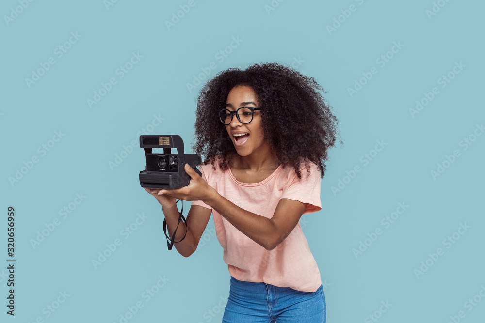 Freestyle. African girl in glasses standing isolated on gray taking photo with instant camera smiling playful