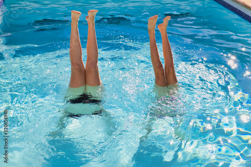 two girls are doing handstand in a swimming pool in the summer