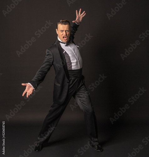 a full-length man on a black background waving his arms in a tuxedo or black 