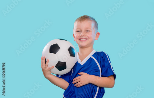 Happy little kid in sportswear holding a soccer ball isolated on blue background © Augustas Cetkauskas