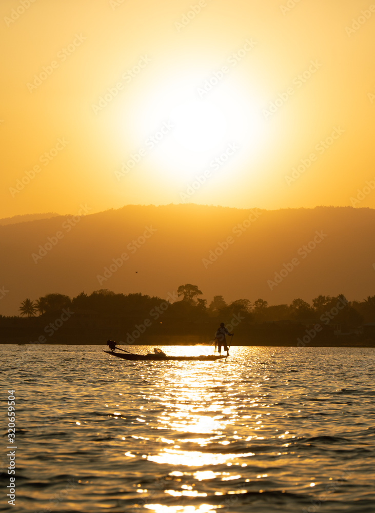 Fisherman with a boat sails over Inle Lake at sunset