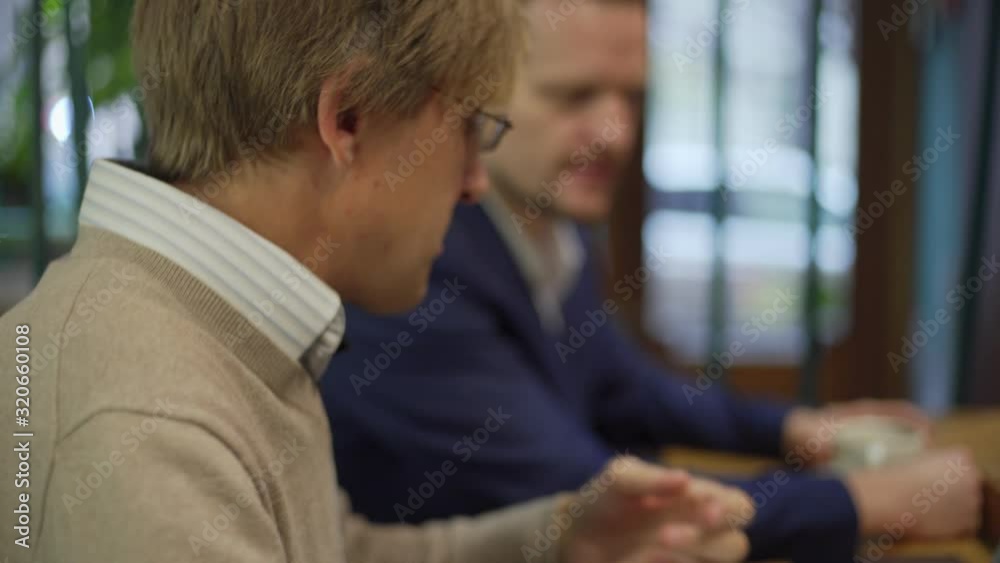 Rack focus tilt down closeup of middle aged programmer explaining project details to business partner land showing code on laptop screen while meeting over coffee at cafe table Rack focus tilt down closeup of middle aged programmer explaining project details to business partner land showing code on laptop screen while meeting over coffee at cafe table