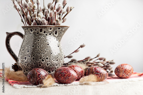 Easter still life with Pysanka and willow branches in ceramic jug on traditional Ukrainian cloth. Decorated Easter eggs, traditional for Eastern Europe culture