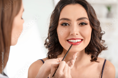 Makeup artist working with beautiful young woman in salon