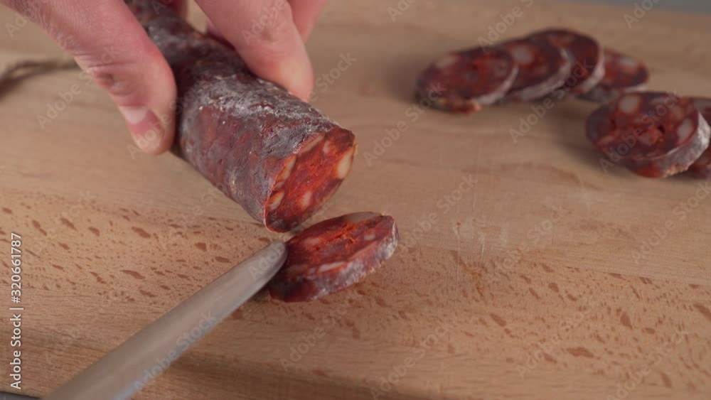 Slicing spanish traditional homemade chorizo sausages into pieces on a wooden cutting board in the kitchen