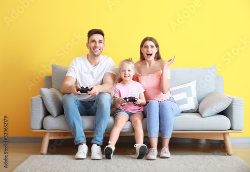 Young family playing video games while sitting on sofa near color wall © Pixel-Shot