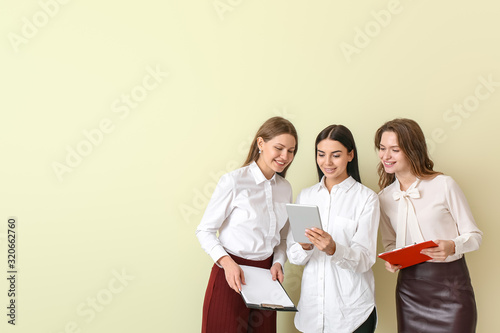 Beautiful young businesswomen with tablet computer on color background