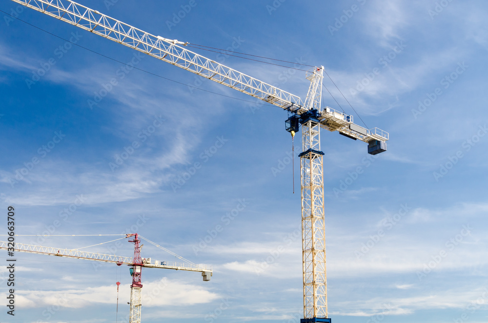 High-rise building under construction. The site with cranes against blue sky with white clouds High-rise building under construction. The site with cranes against blue sky with white clouds