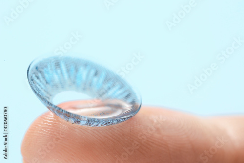 Human finger with contact lens on color background, closeup
