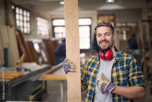 Portrait of handsome smiling carpenter with wood material at workshop holding thumbs up. Do it yourself concept. Creativity concept. photo