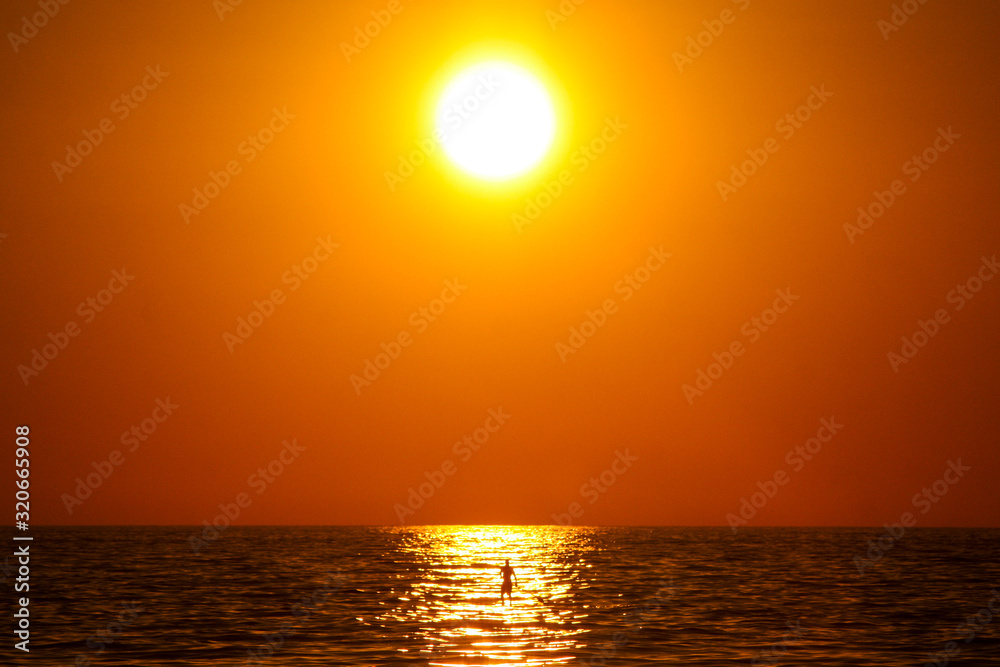 Sunny evening on a beach in Puerto Escondido, Mexico, with a man on a SUP board paddling under the sun. Concept of an enjoyment under the sun.