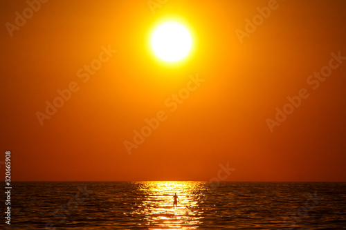 Sunny evening on a beach in Puerto Escondido, Mexico, with a man on a SUP board paddling under the sun. Concept of an enjoyment under the sun. © Anze