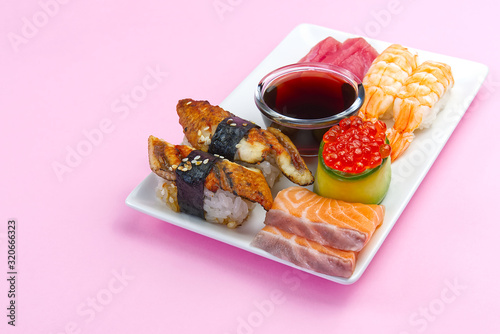 traditional japanese sushi set on a white plate isolated on a pink background. tasty set of sushi, nigiri, sahimi and maki. delicious dinner or lunch for one person. photo