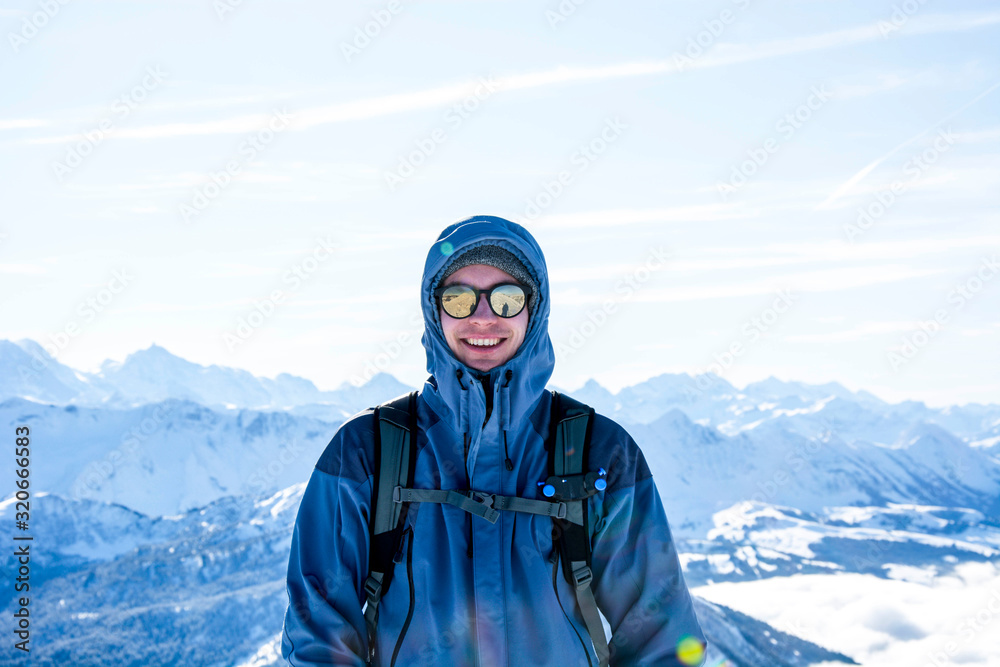 mountaineer backpacker smiling at the summit against blue snowy mountain layers in winter. sunny, blue sky