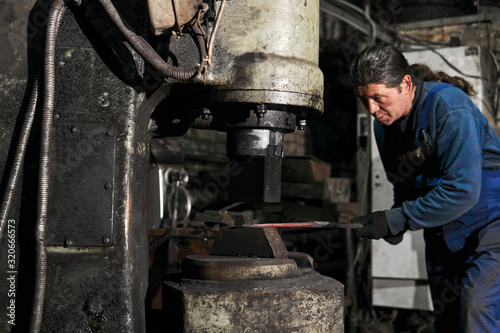 blacksmith processes a hot workpiece with a machine hammer