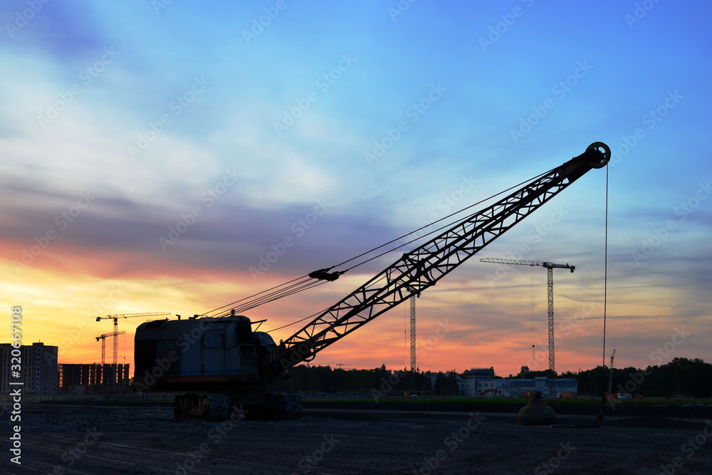 Large crawler crane or dragline excavator with a heavy metal wrecking ball on sunset background. Wrecking balls at construction sites. Dismantling and demolition of buildings and structures