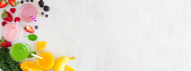 Assorted healthy smoothies. Overhead view corner border banner against a marble background. Blueberry, strawberry, green and orange. Copy space.