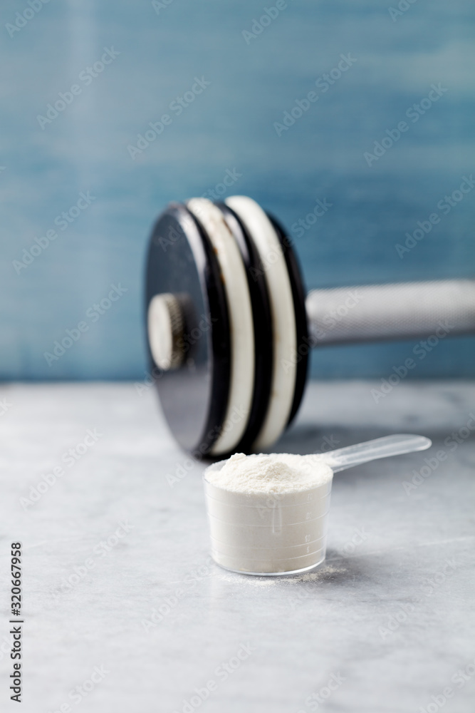 Scoop of Whey Protein and a dumbbell. Bodybuilding food supplements on stone / wooden background. Close up. Copy space. Scoop of Whey Protein and a dumbbell. Bodybuilding food supplements on stone / wooden background. Close up. Copy space.