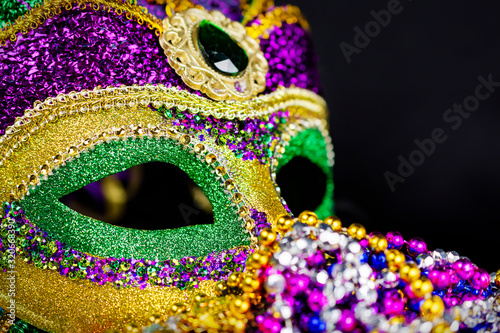 Close up view of a jester mask with colored beads blurred in the foreground. Black background.