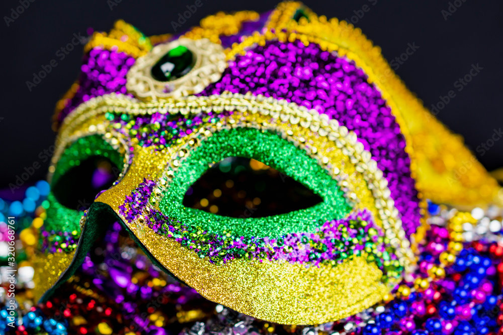 A close up view of a colorful jester mask.  Selective focus on the front edge of mask falling off into blurriness.  Dark background.  Landscape cropped.