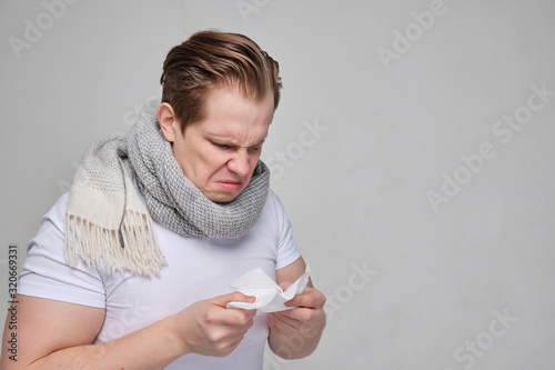 A man with a white T-shirt blew his nose in a handkerchief. The concept of the disease of the common cold, flu. close up. photo