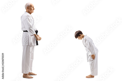 Boy in karate kimono bowing in front of his elderly karate instructor