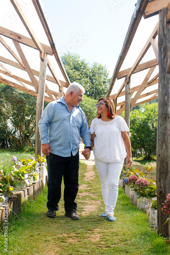 Adult Hispanic couple walking hand in hand in a nursery - couple smiling in a garden - senior marriage