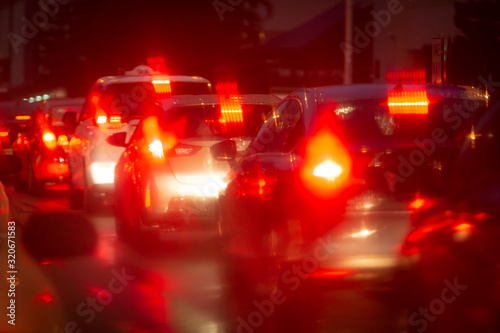 Cars in night traffic jam with abstract bokeh caused by rain drops reflecting onto car windscreen. Rows of blurred red car brake lights on a city street. Indistinct focus applied.