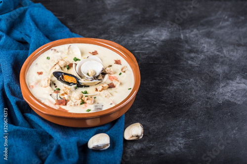 Clam chowder in a brown plate. The main ingredients are shellfish, broth, butter, potatoes and onions.