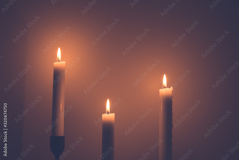 Background or texture of large white burning candles in dark room over wall background. Background or texture of large white burning candles in dark room over wall background.