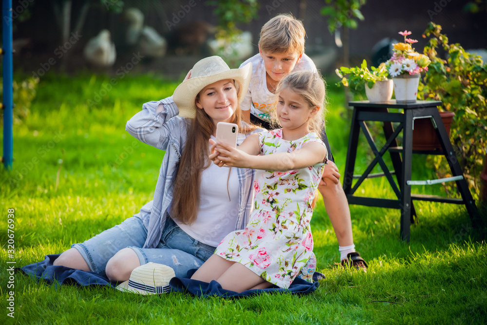Fototapeta premium Young mother with pretty daughter and handsome son make photo in backyard
