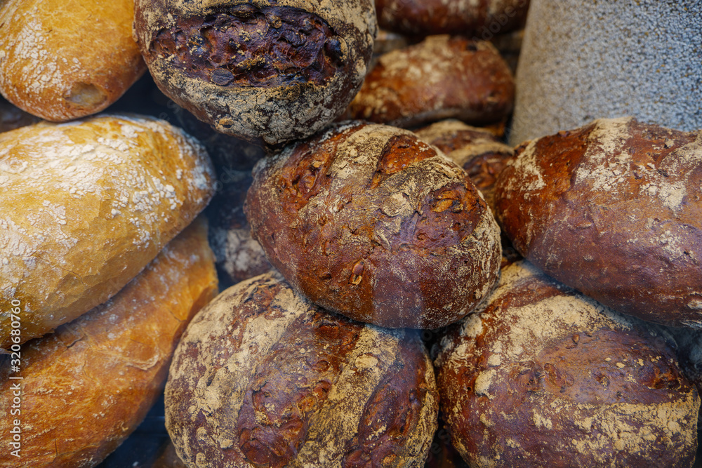 Heap and stack of round rye and wheat of rustic and crusty breads at display of bakery store. 