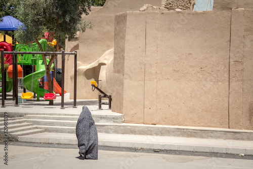 Bild auf Leinwand Shape of a woman walking in the streets of Yazd, Iran, passing near a children p
