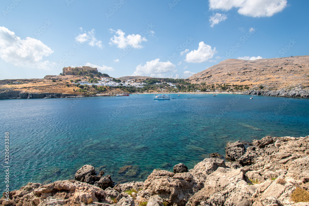Lindos bay with boats, white houses of village of Lindos and Acropolis in background (Rhodes, Greece)