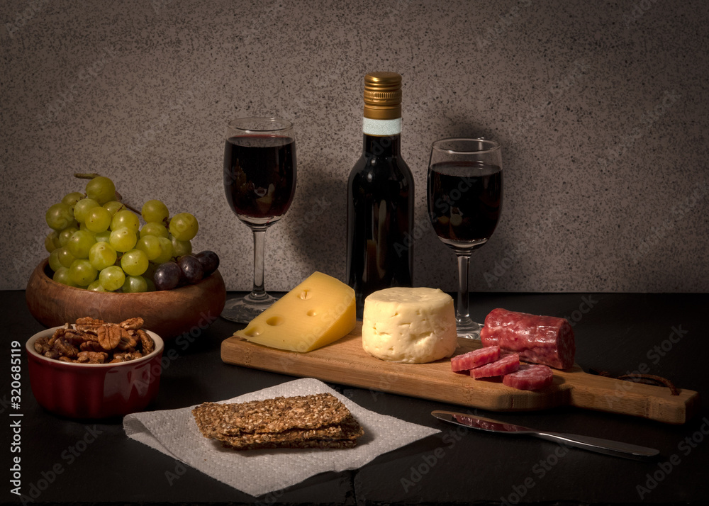 Cheese board for two with grapes, red wine and crackers, viewed from the side, with salami Cheese board for two with grapes, red wine and crackers, viewed from the side, with salami