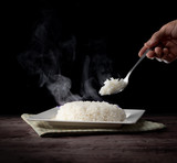 White steam rice with hand holding spoon eating hot rice over dark background