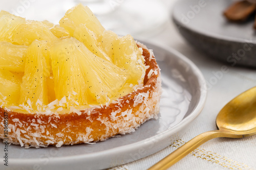 Small pineapple tart or tartlet with glazed pineapple fruit pieces and grated coconut by a golden spoon, over a white and gold table cloth. photo